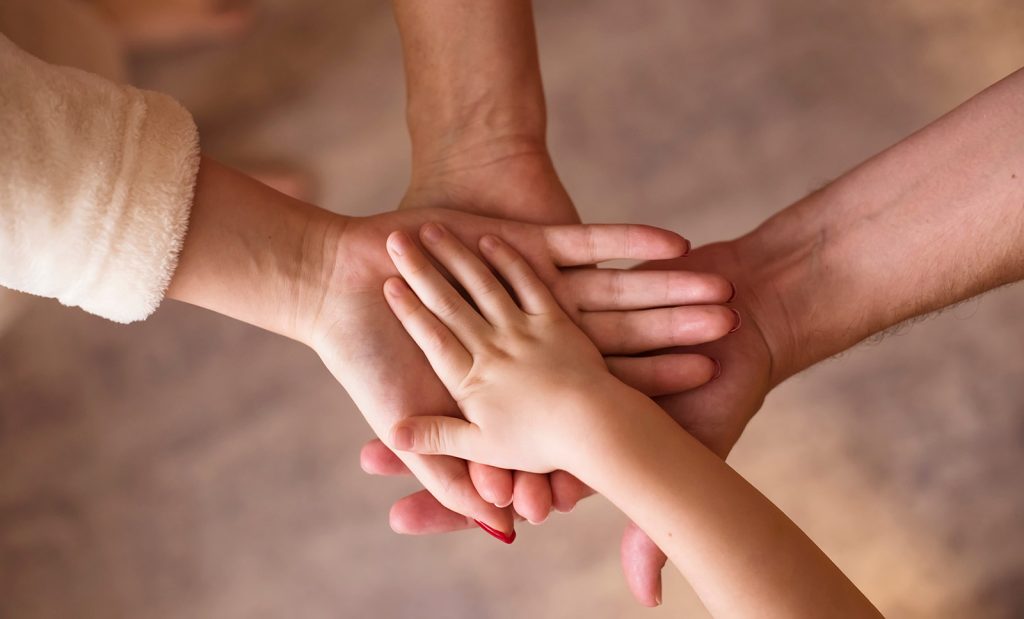 Four hands together, indicating a child and parents or caregivers